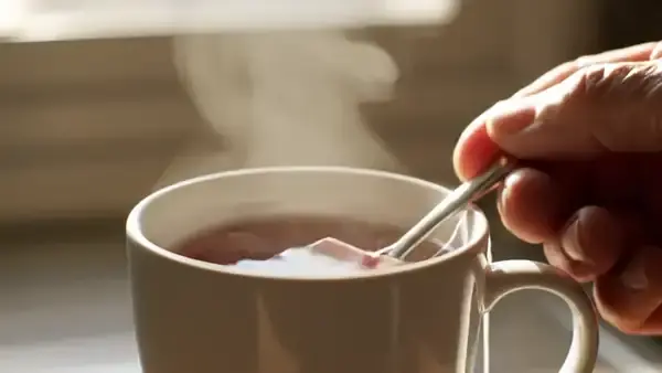 A hand pressing a tea bag against the side of a mug of red tea with a spoon