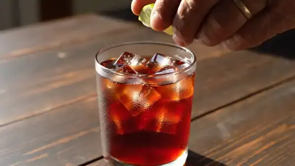 Fingers squeezing a lime wedge over a tall glass of red iced tea
